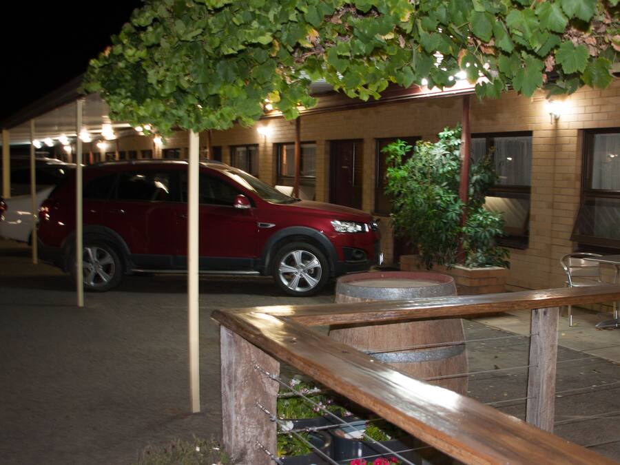 Een rode SUV geparkeerd in een overdekte buitenruimte met een houten bank en potplanten.