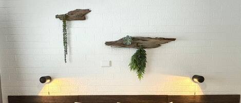 Una cama con cabecera de madera oscura, dos almohadas, una almohada a cuadros y una caja de pañuelos en una mesita de noche.