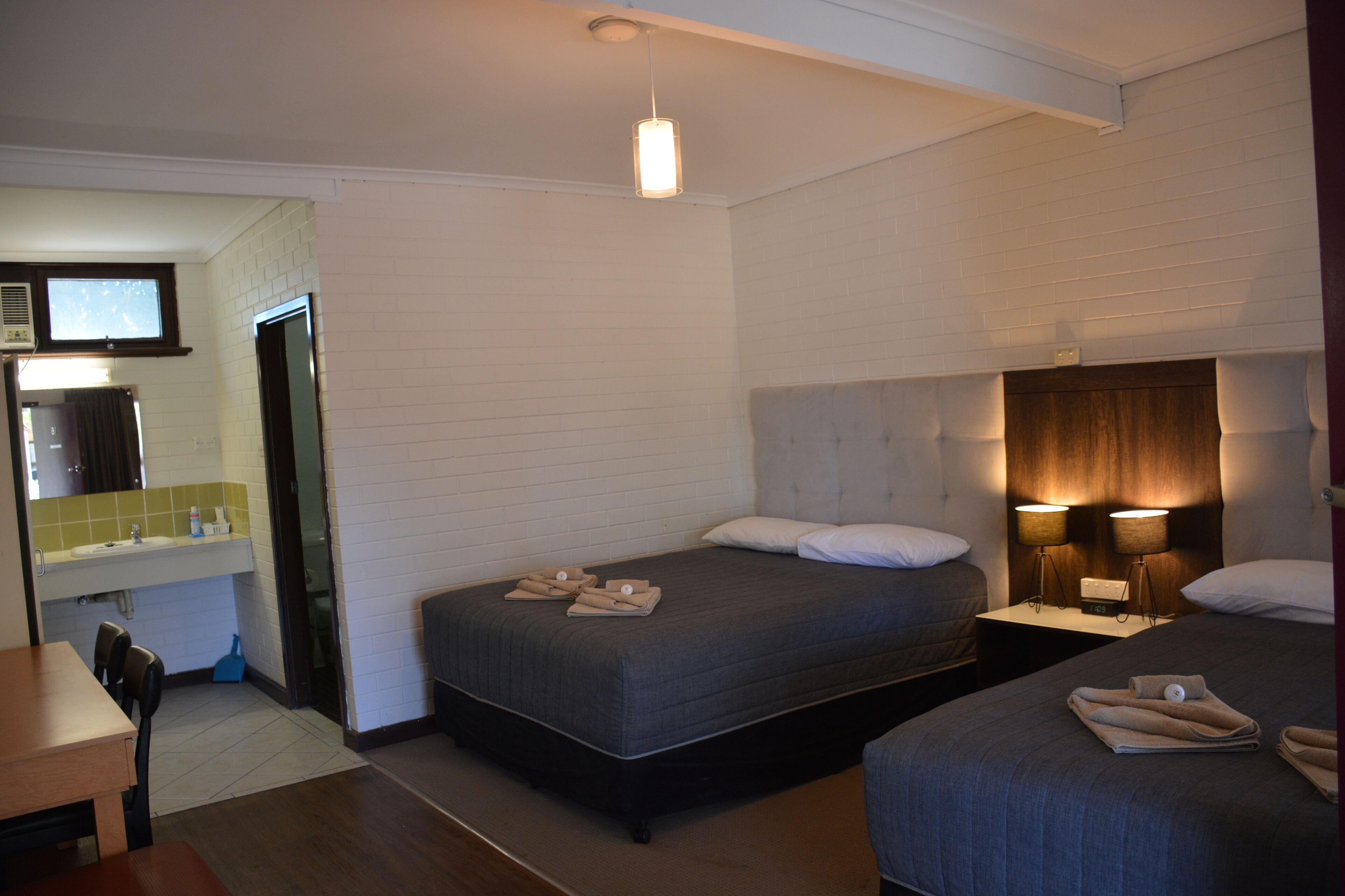 A hotel room with two beds, a bathroom, and a dining area.