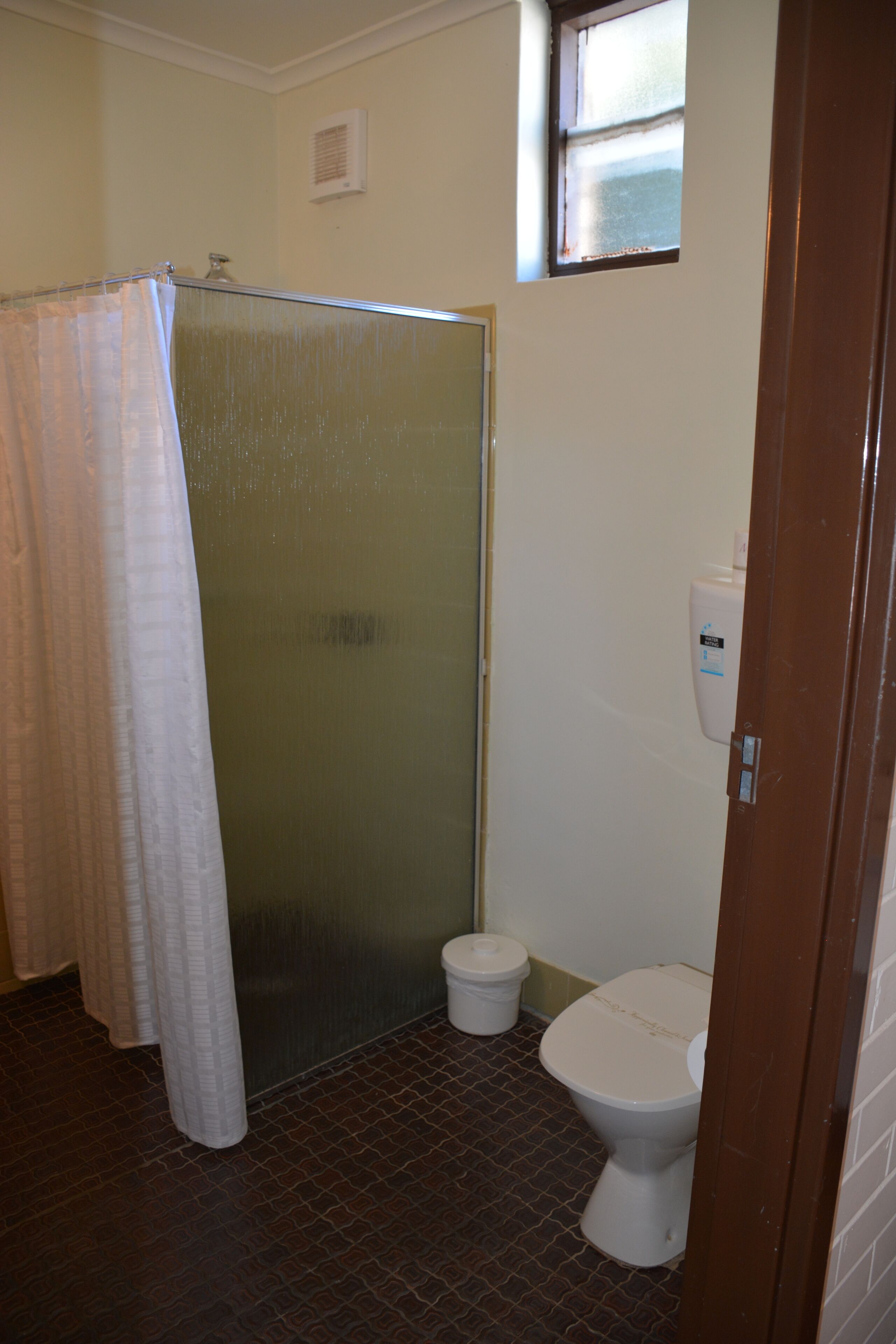 A bathroom with a shower, toilet, and a window.