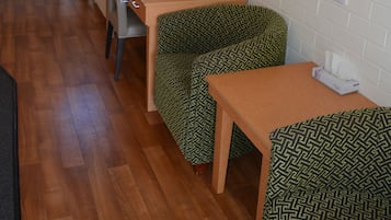 A compact room with a wooden floor, a small table, a chair, a sofa, a TV mounted on the wall, and a window.