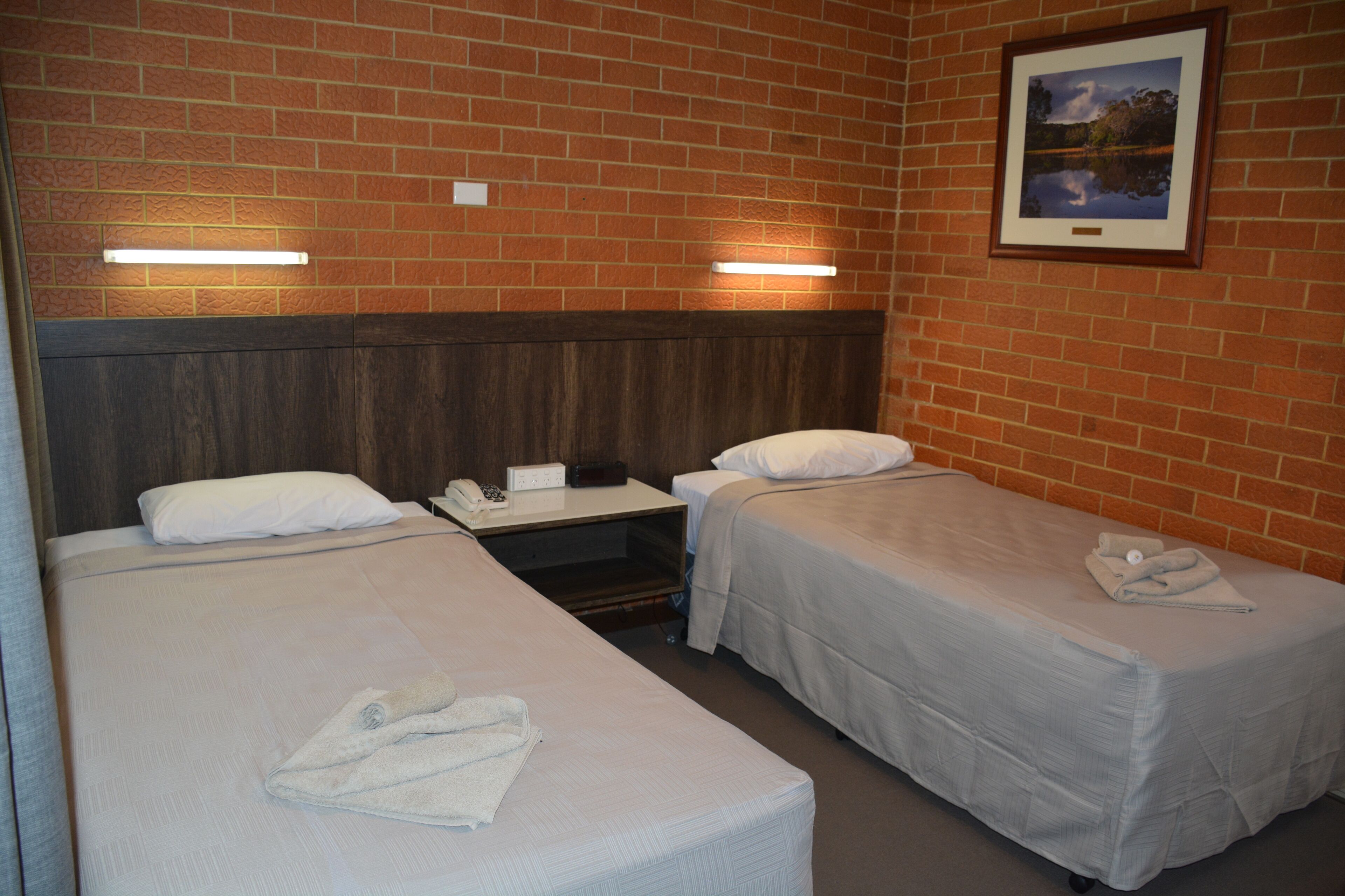 Una habitación de hotel con dos camas, un cabecero de madera, una mesita de noche y un cuadro enmarcado en la pared.
