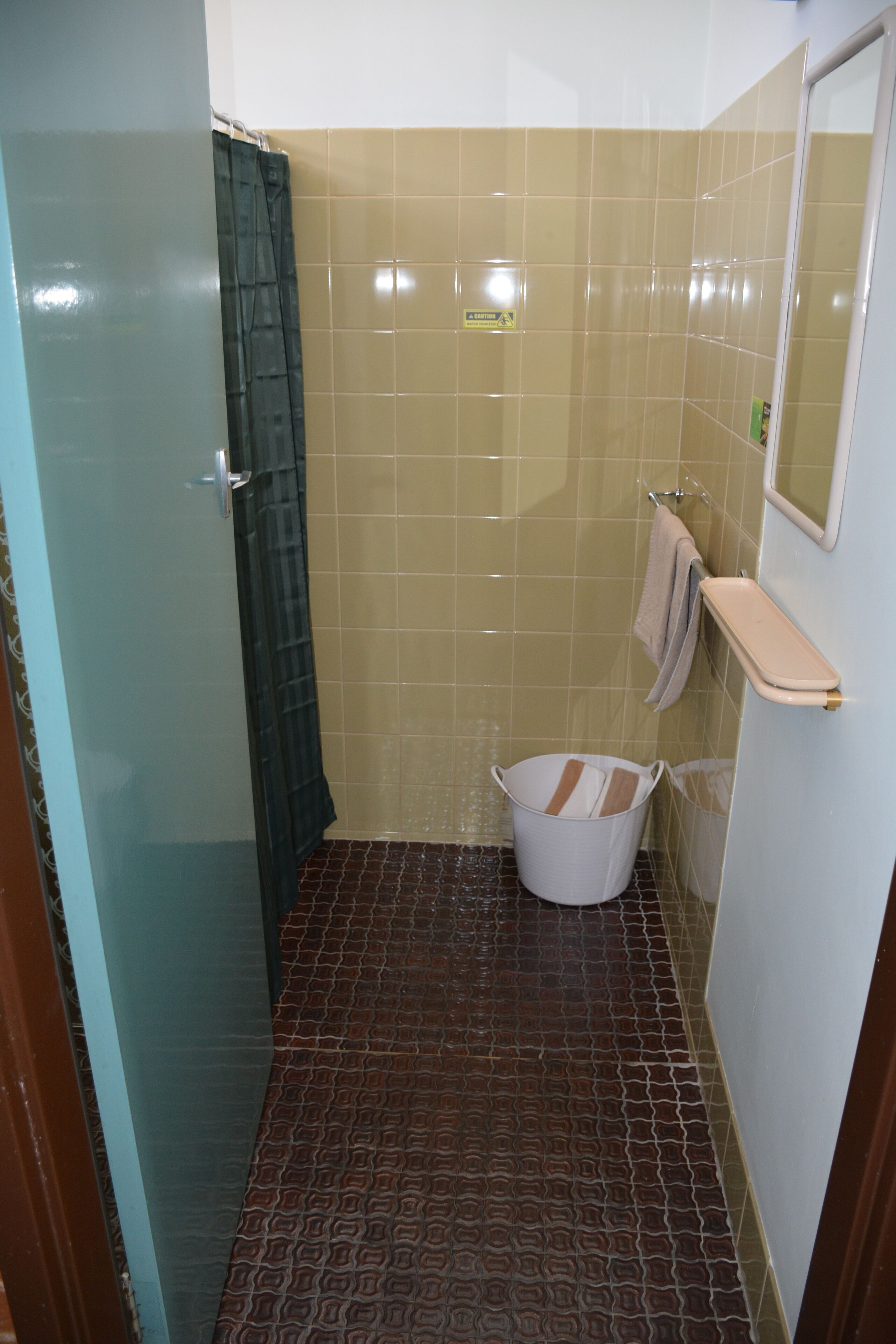 A bathroom with a shower, a towel rack, and a trash bin.