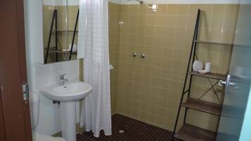 A bathroom with a white sink, a mirror, a shower with a glass door, and a shelf with toiletries.