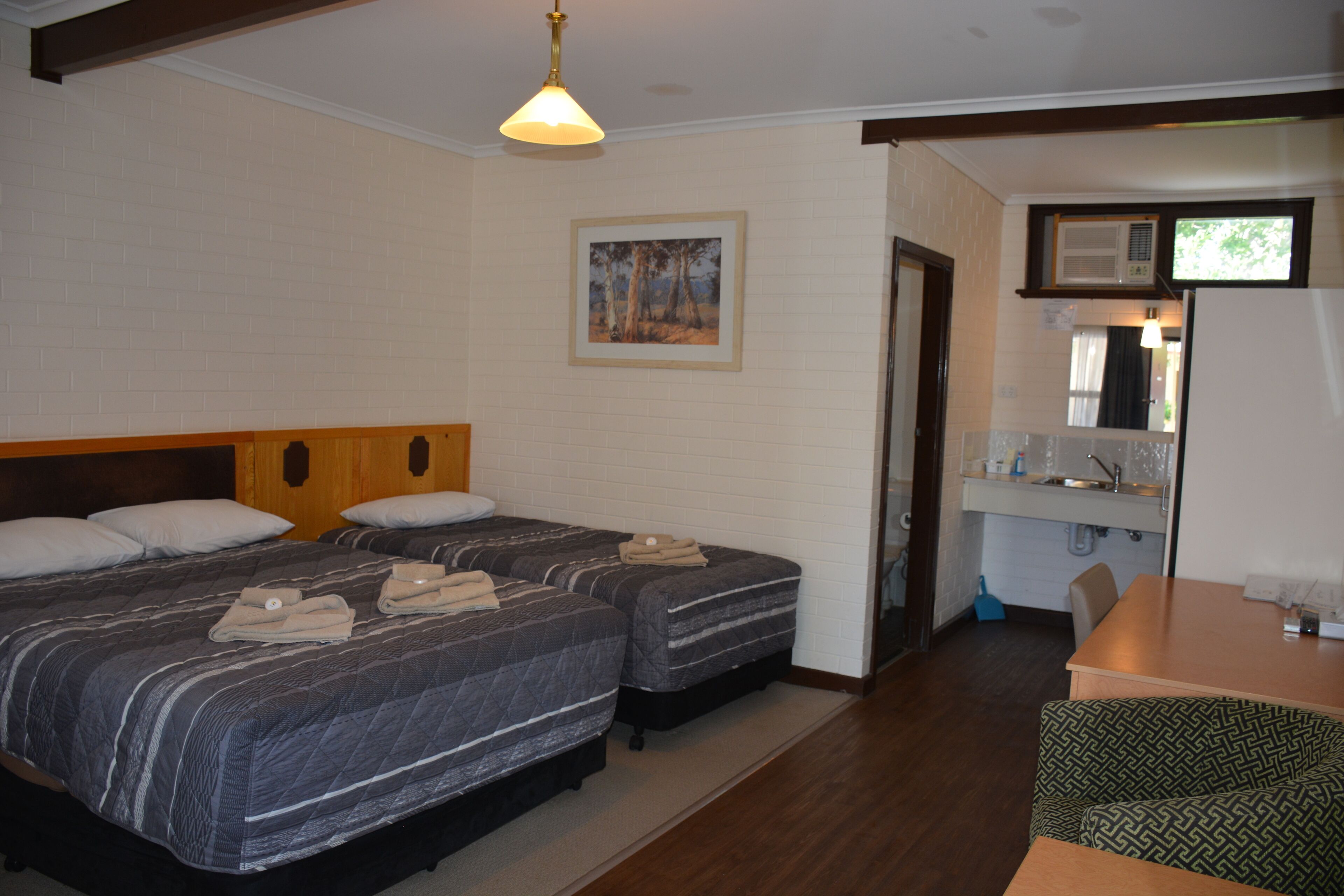 A hotel room with two beds, a small kitchenette, and a dining area.