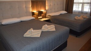 Habitación de hotel con dos camas, cada una con cabecera, mesita de noche con lámparas y toallas sobre las camas.
