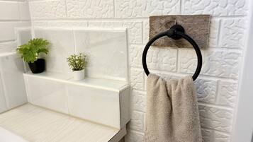 Un baño con azulejos blancos con textura, un perchero de madera y dos plantas en macetas sobre una repisa.