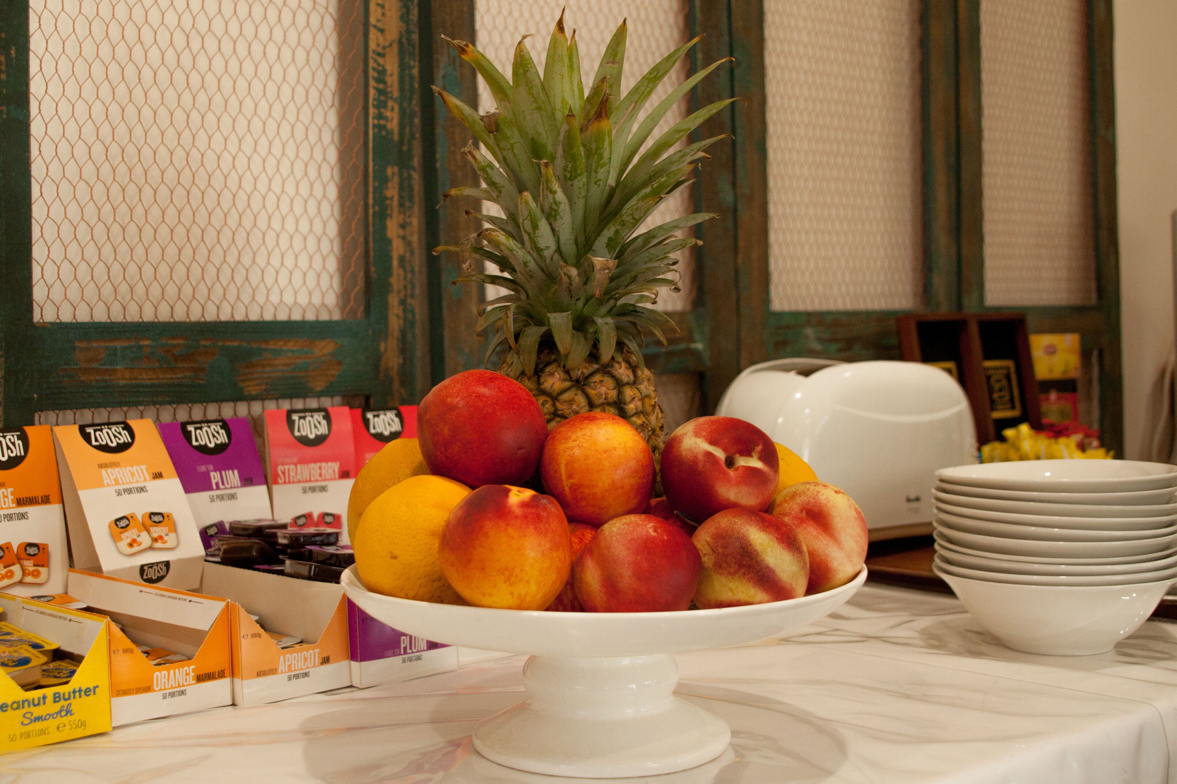 A fruit bowl with a pineapple and peaches on a marble table, surrounded by boxes of ZOOSA snacks.