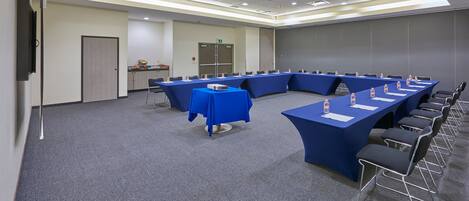 A conference room with multiple tables and chairs, equipped with water bottles and papers, and a projector on one table.