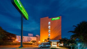 Un hotel CityExpress Junior con un diseño moderno, que presenta un letrero llamativo y una camioneta estacionada frente a él.