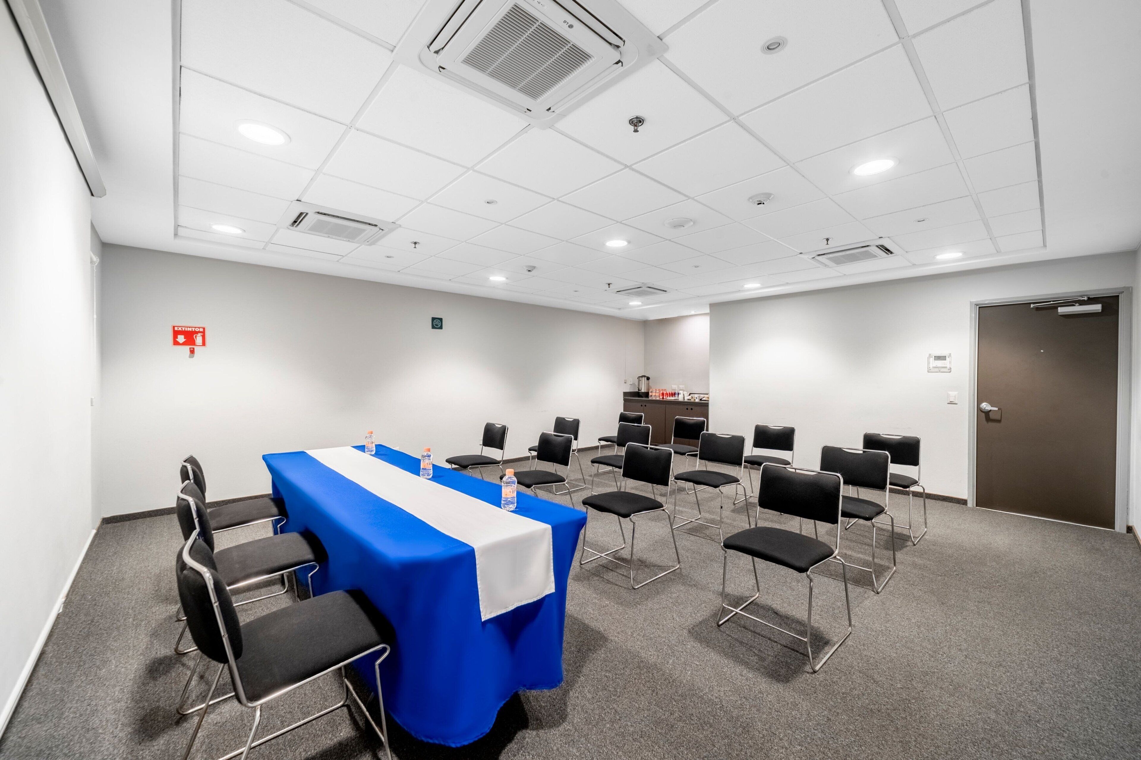 A conference room with a blue table, black chairs, and a white tablecloth.