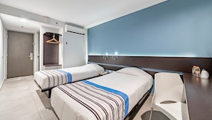 Habitación de hotel con dos camas, un escritorio, una silla, un armario y la puerta del baño.