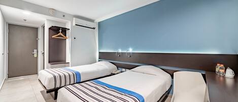 Een hotelkamer met twee bedden, een bureau, een stoel, een kledingkast en een badkamedeur.