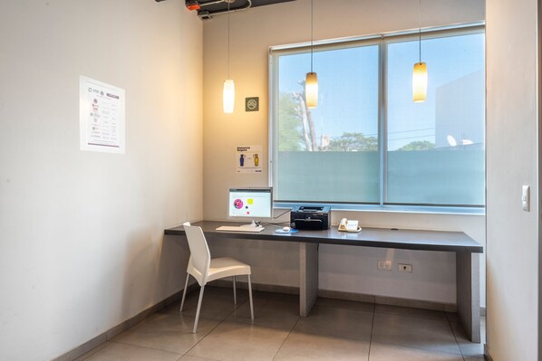 Un espacio de oficina moderno con un escritorio, computadora y silla. Hay una ventana con vistas a árboles y un letrero en la pared.