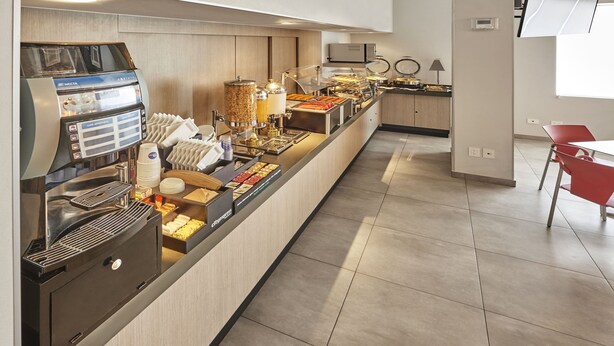 Una barra de desayuno con una máquina de café, diferentes alimentos y una zona de estar con una silla roja.