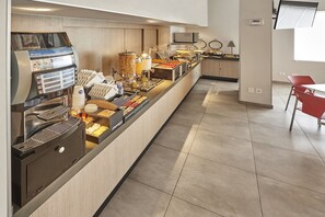 A breakfast bar with a coffee machine, various food items, and a seating area with a red chair. - City Express Junior by Marriott Ciudad Del Carmen (Ciudad del Carmen)