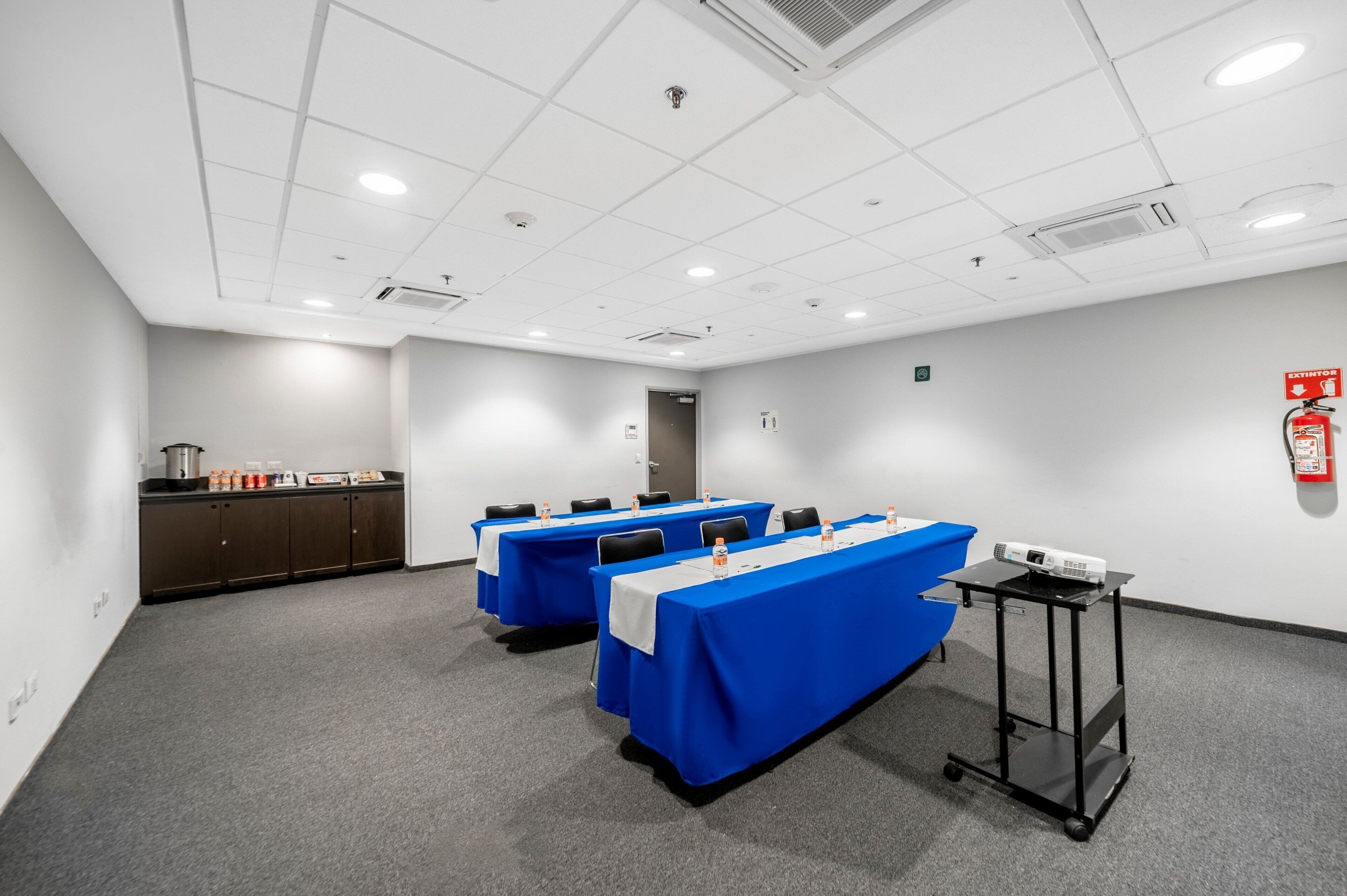 Un salón de conferencias con tres mesas, un proyector y un extintor.