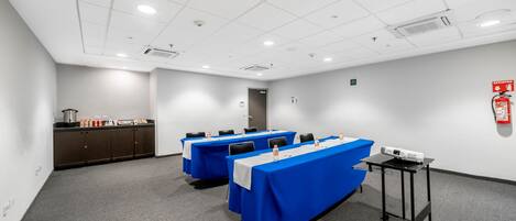 Un salón de conferencias con tres mesas, un proyector y un extintor.