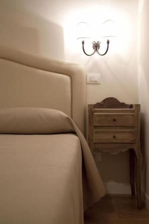 Un dormitorio con cama, mesita de noche de madera y lámpara de pared.
