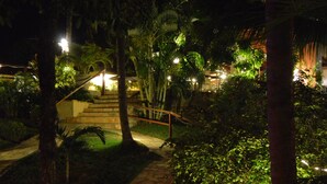 A nighttime garden pathway with stone steps leading to a staircase, surrounded by lush greenery and palm trees. - Pousada Cavalo Marinho (Tibau do Sul)