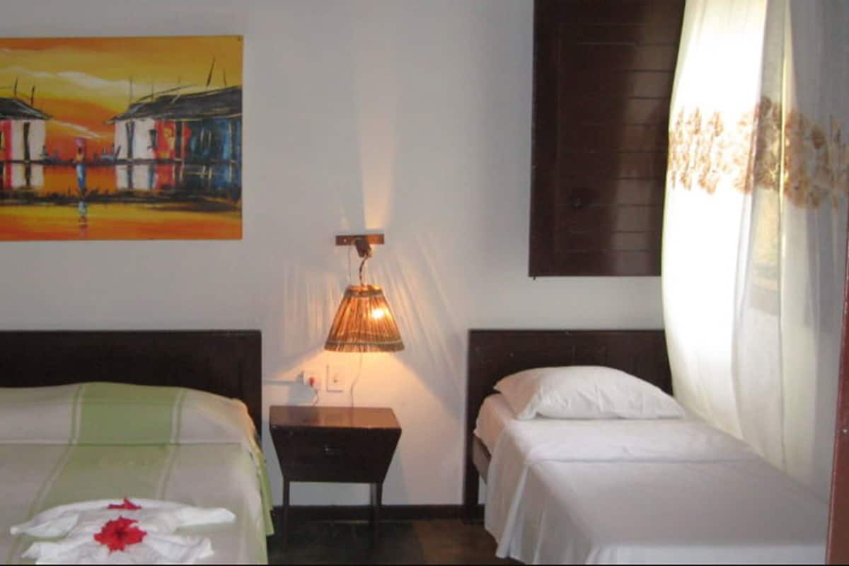 Quarto de hotel com duas camas, um quadro na parede, uma luminária e uma janela com cortinas.