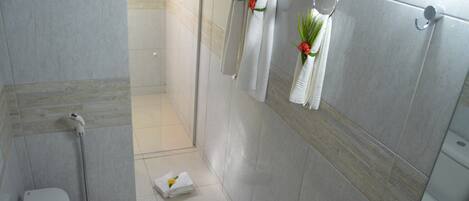 A bathroom with a shower, toilet, and towel rack with towels and a plant.