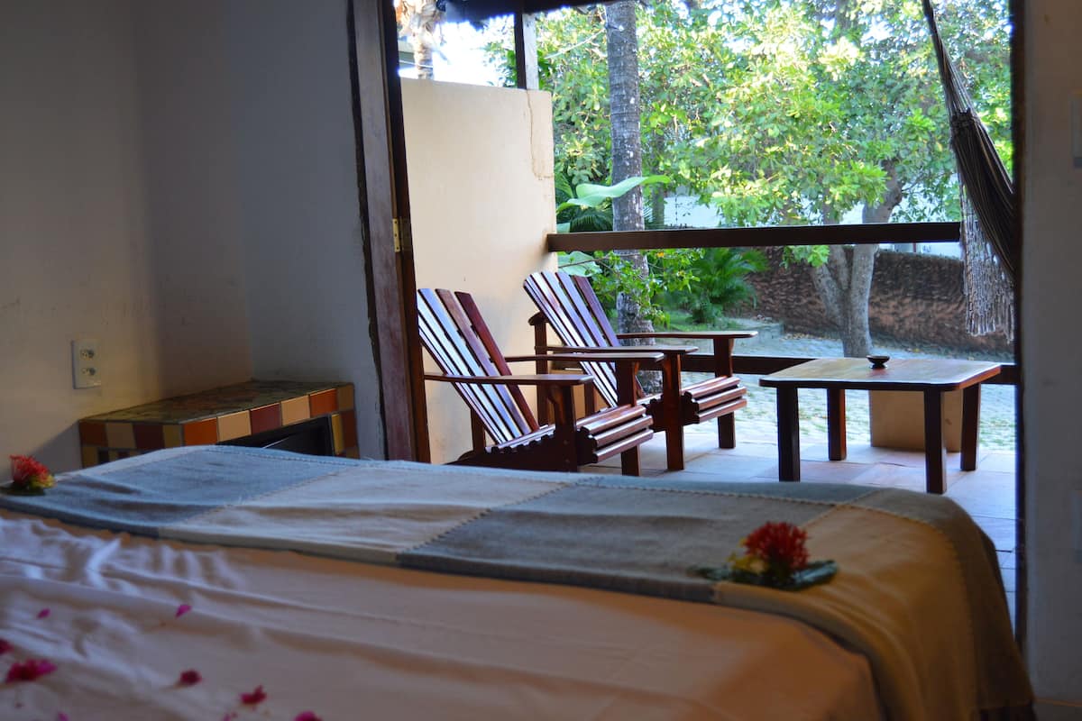 Um quarto com uma cama, duas cadeiras listradas, uma mesinha e vista para um jardim.