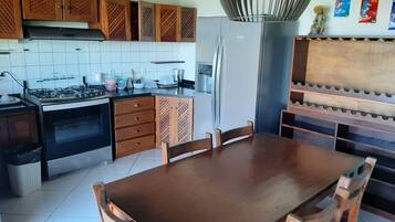 A kitchen with wooden cabinets, a gas stove, a refrigerator, and a dining table with chairs.