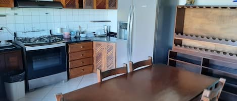 A kitchen with wooden cabinets, a gas stove, a refrigerator, and a dining table with chairs.