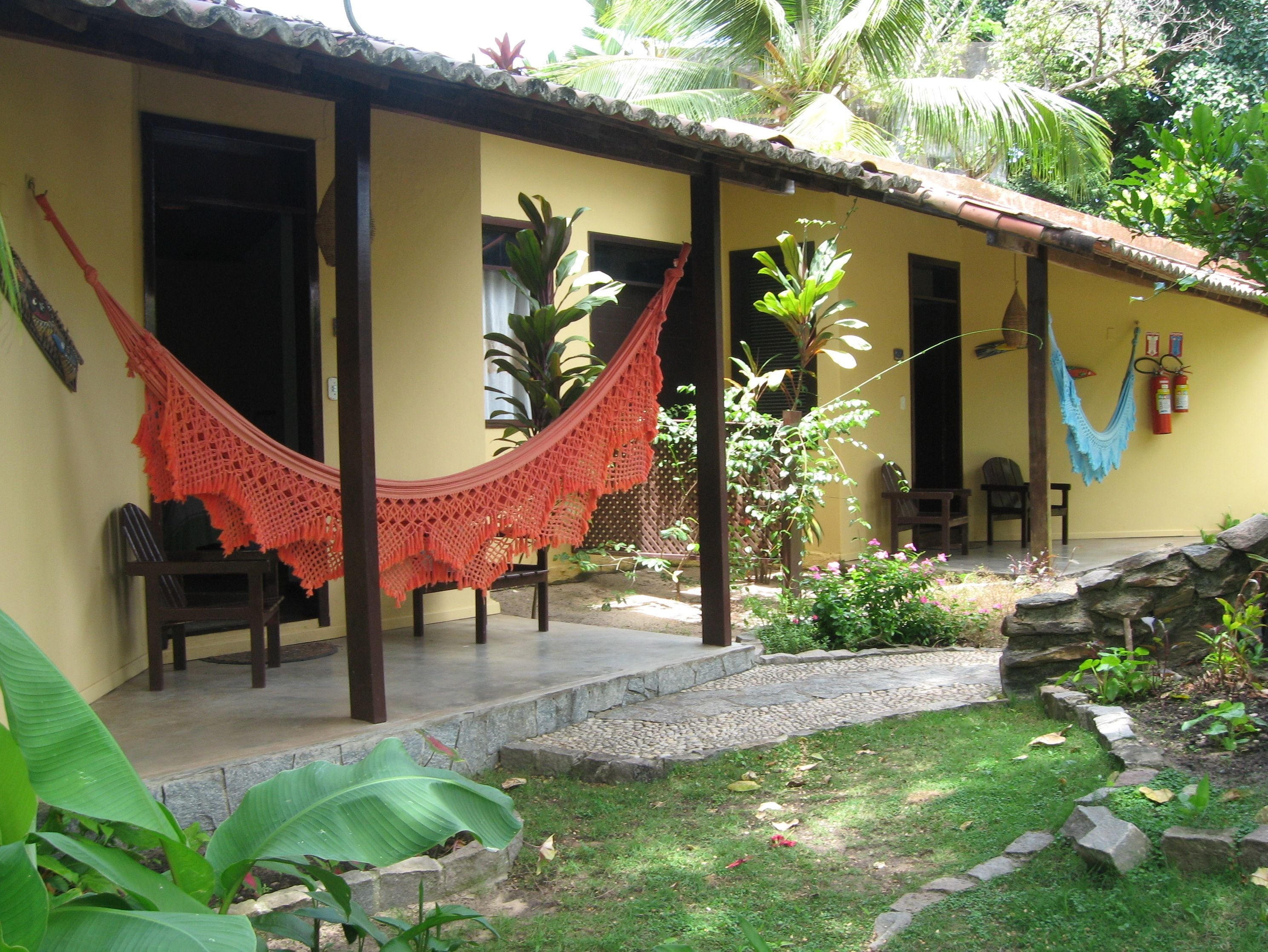 A yellow building with a porch, two hammocks, and a stone wall.
