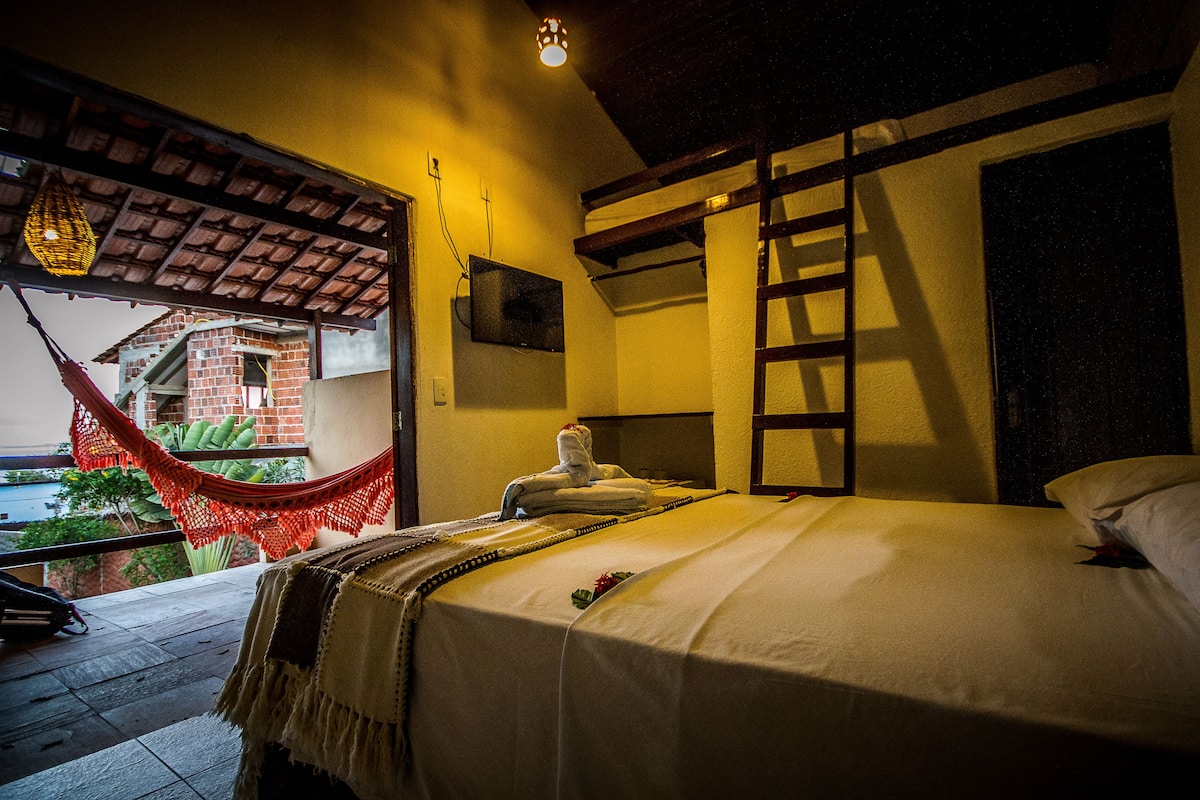 Quarto com cama, rede, televisão e vista para um edifício lá fora.