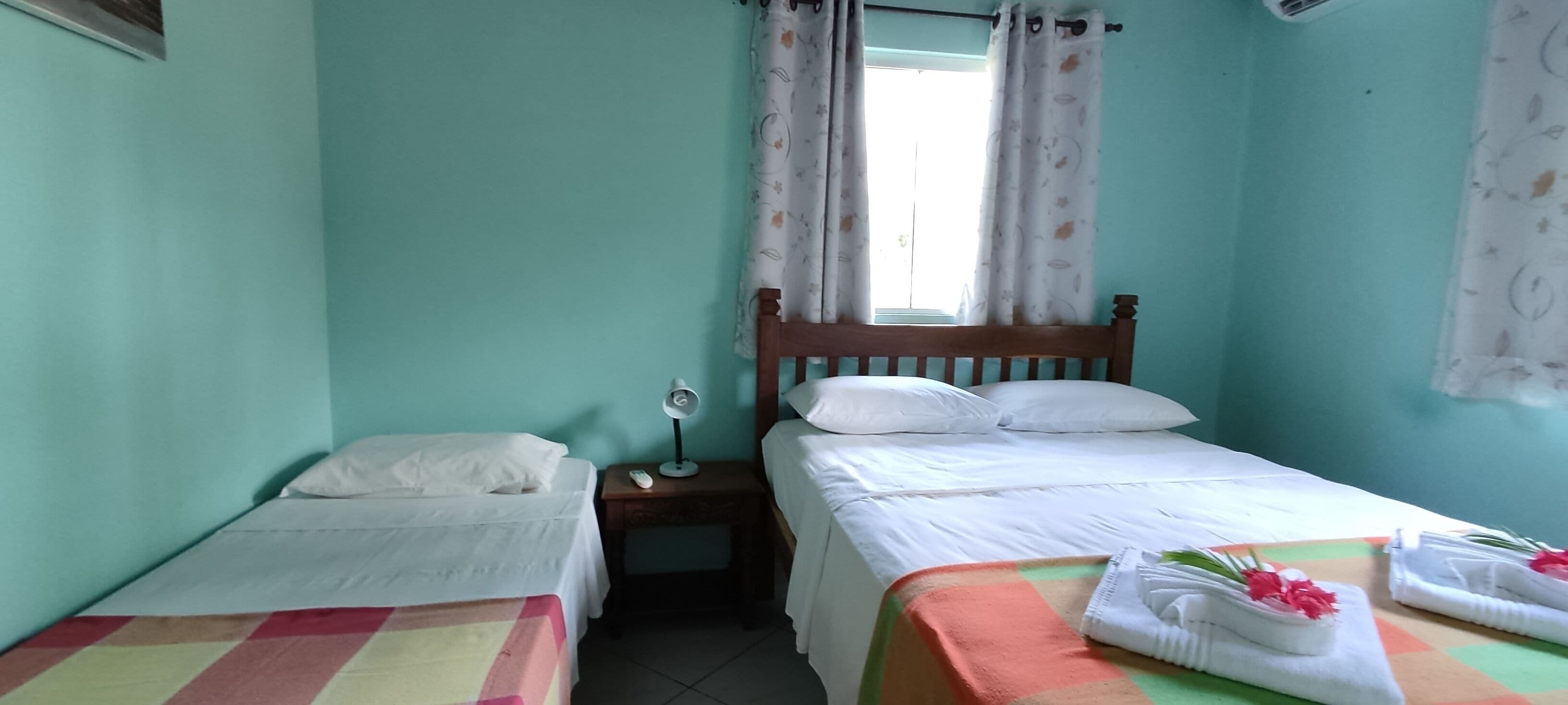 Una habitación con dos camas individuales, una mesita de noche con lámpara y una ventana con cortinas.