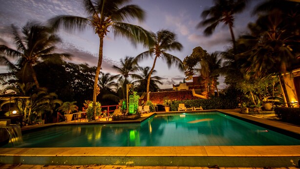 A swimming pool surrounded by palm trees and a building with a tiled roof. - Pousada Cavalo Marinho (Tibau do Sul)