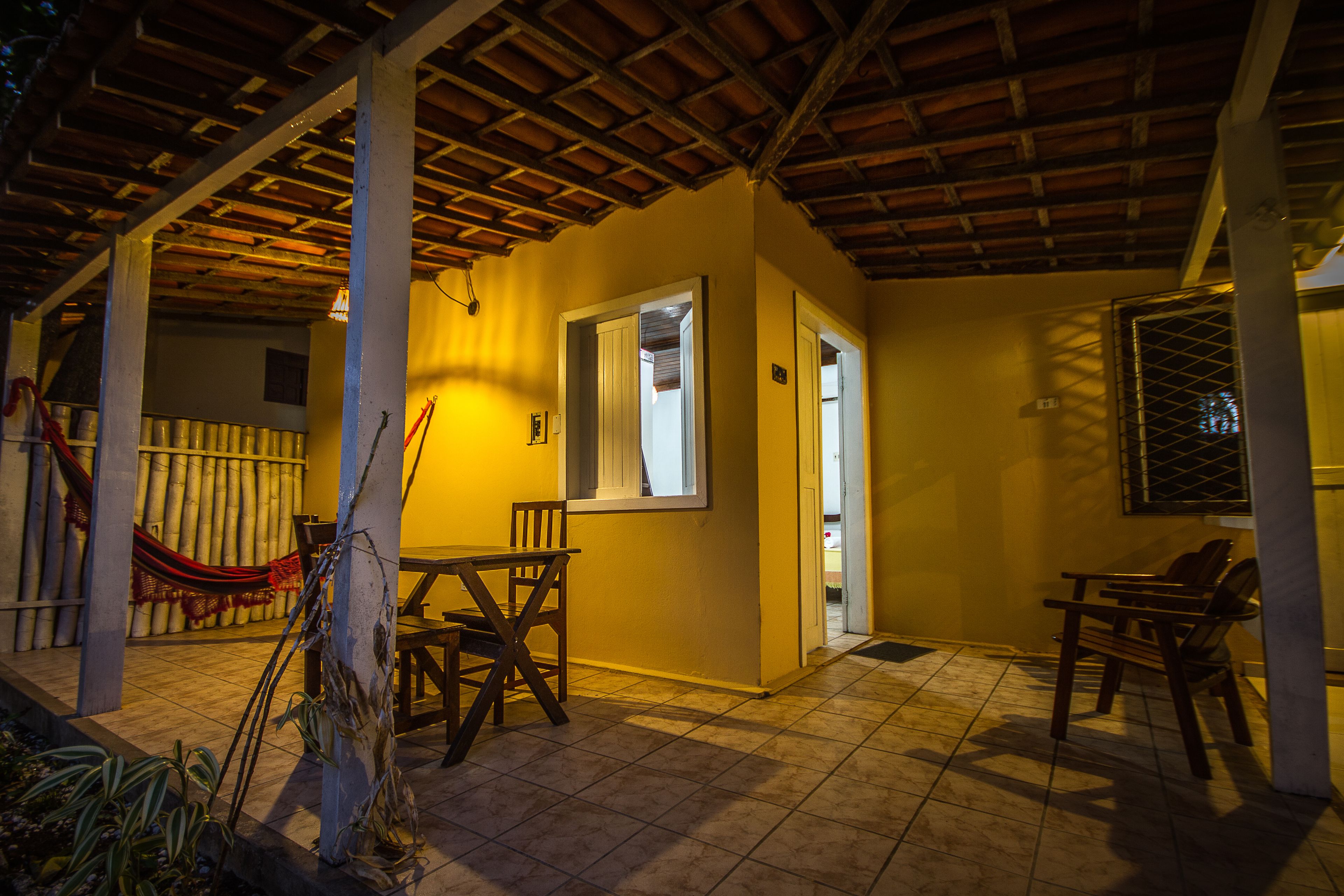 A covered patio area with a table and chairs, a hammock, and a door leading to another room.