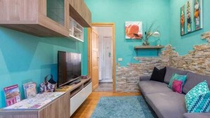 A living room with teal walls, a grey sofa, a TV, and a stone wall feature. - Domus Domas & Boutique   (Rome)