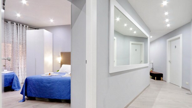A modern hotel room with a large bed, a bedside table, a mirror, and a bench. - Domus Domas & Boutique   (Rome)
