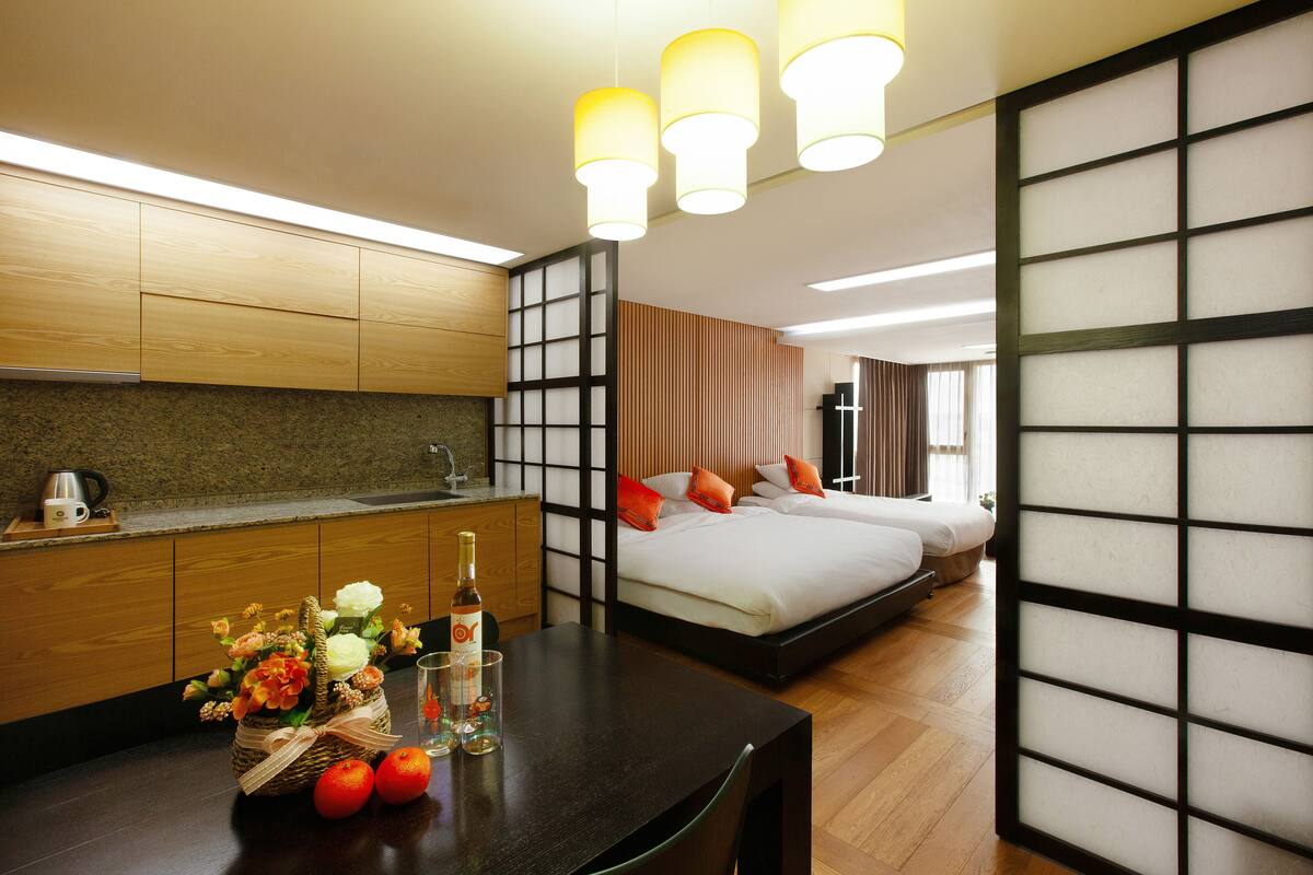 A hotel room with a wooden dining table, a bed with pillows, a sofa bed, and a traditional sliding door.