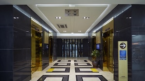 Un hall d’hôtel moderne avec un ascenseur central, des panneaux d’orientation et une plante en pot.