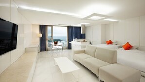 Une chambre d’hôtel moderne dotée d’un grand téléviseur à écran plat, d’un canapé, d’un lit avec des oreillers orange, d’un coin repas avec une table et des chaises, et offrant une vue sur l’océan.
