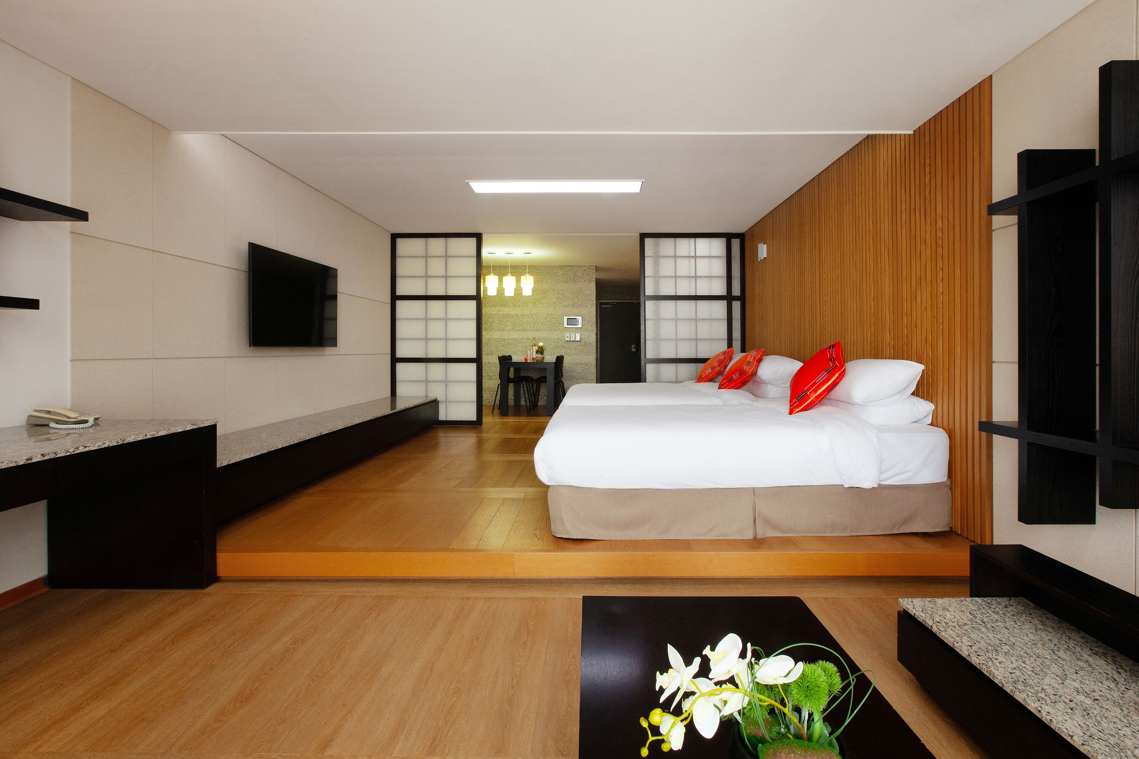 A modern hotel room with a large bed, a bedside table, a TV mounted on the wall, and a wooden floor.