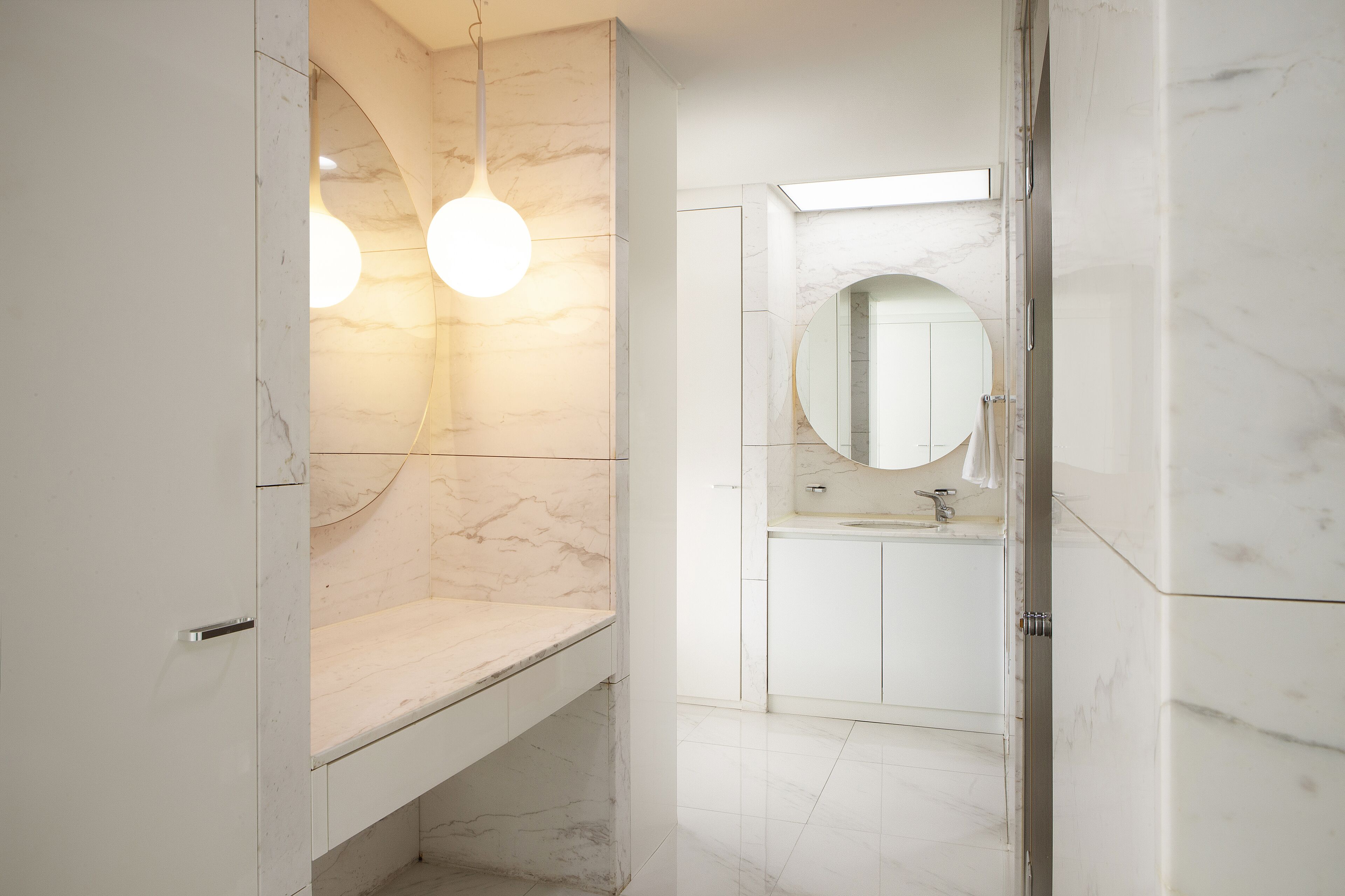 A modern bathroom with marble walls, a round mirror, and two pendant lights.