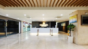 Un espace d’accueil d’hôtel au design moderne, comprenant un comptoir d’accueil, une horloge et une plante en pot.
