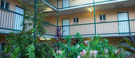 A multi-story building with balconies and a garden area with various plants and flowers.