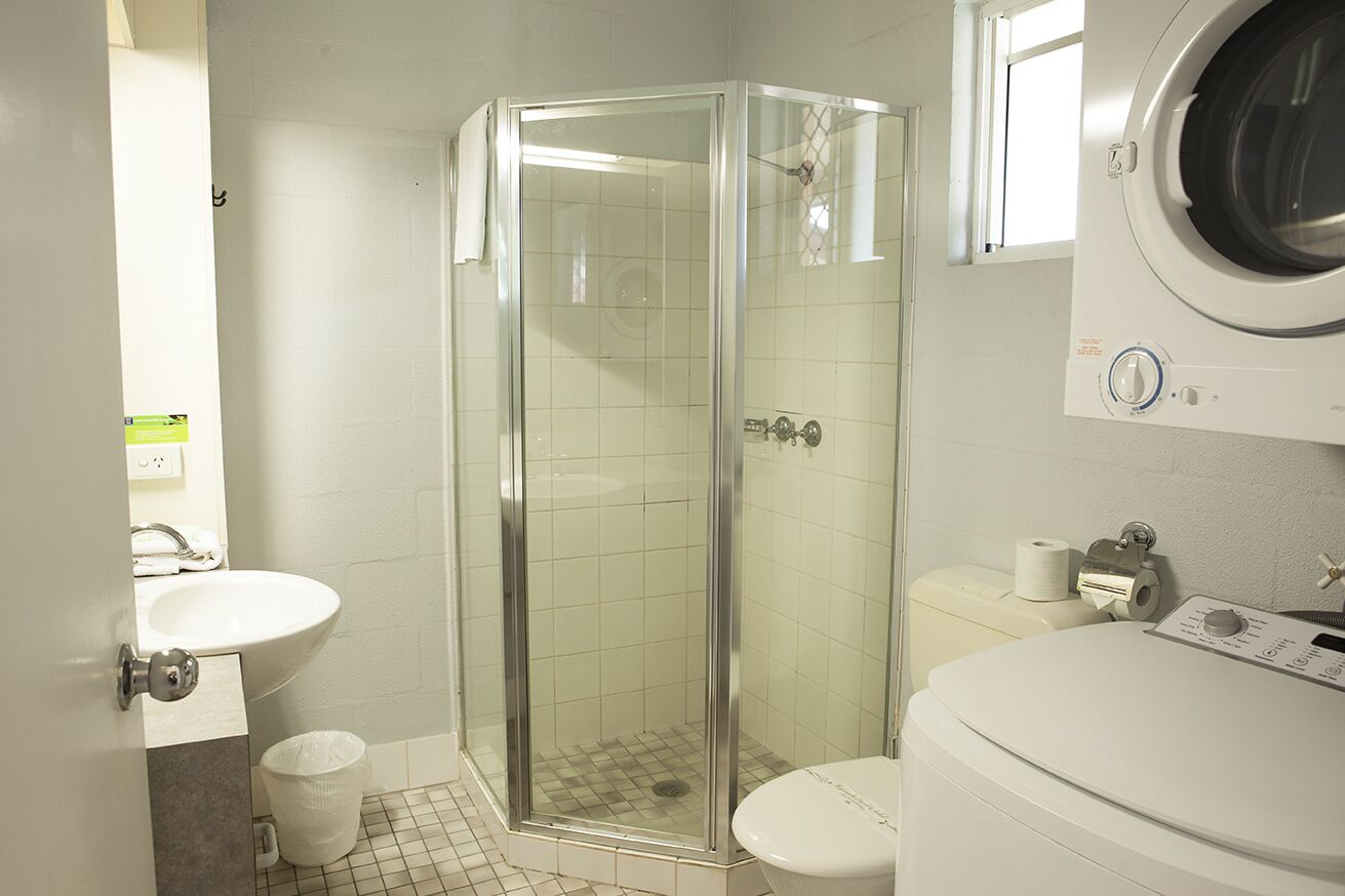 Een badkamer met een douchecabine, wastafel, toilet en een wasmachine.