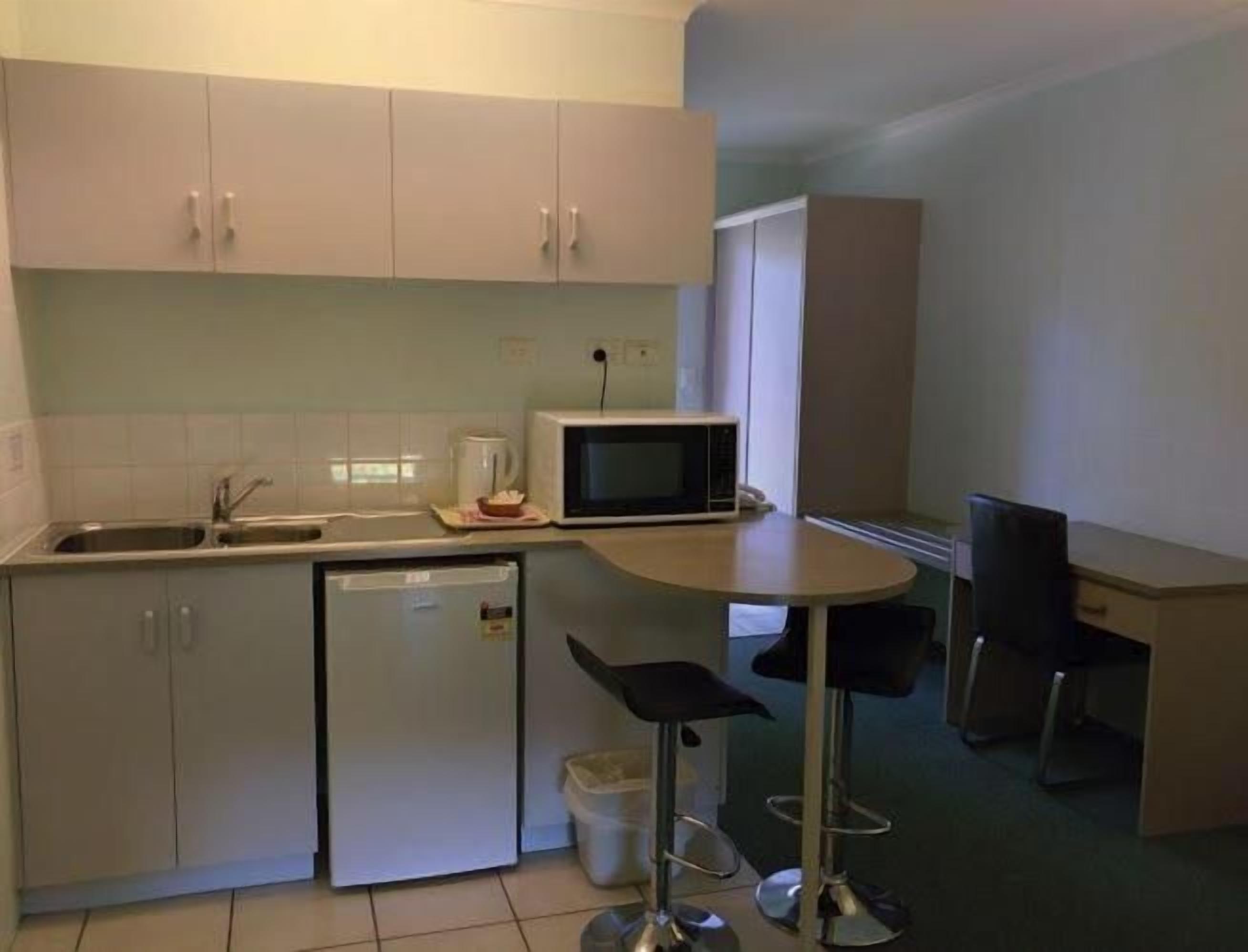 A compact kitchen with a microwave, sink, and a small refrigerator. There is a dining area with a table and two chairs.