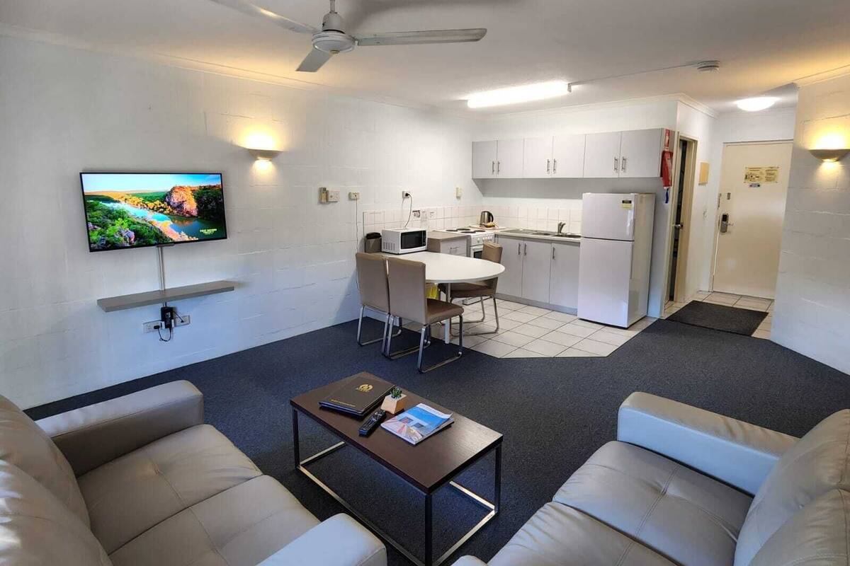 A compact living space with a kitchenette, a dining area, and a seating area with a television mounted on the wall.