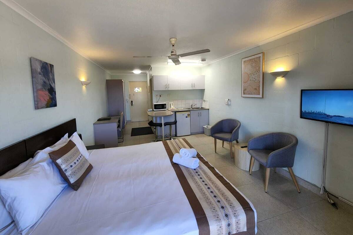 A hotel room with a bed, a desk, a chair, a television, and a kitchenette.