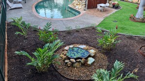 A swimming pool with lounge chairs and a hot tub surrounded by plants and a small garden area. - Alatai Holiday Apartments (Darwin)
