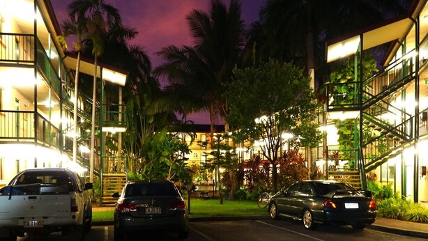 A multi-story hotel with a parking area, surrounded by palm trees and greenery. - Alatai Holiday Apartments (Darwin)