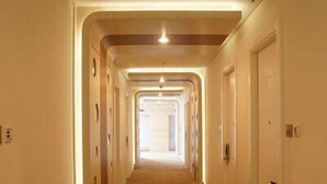 Un long couloir étroit, typique des hôtels, avec un tapis à motifs et une rangée de portes d’un seul côté.